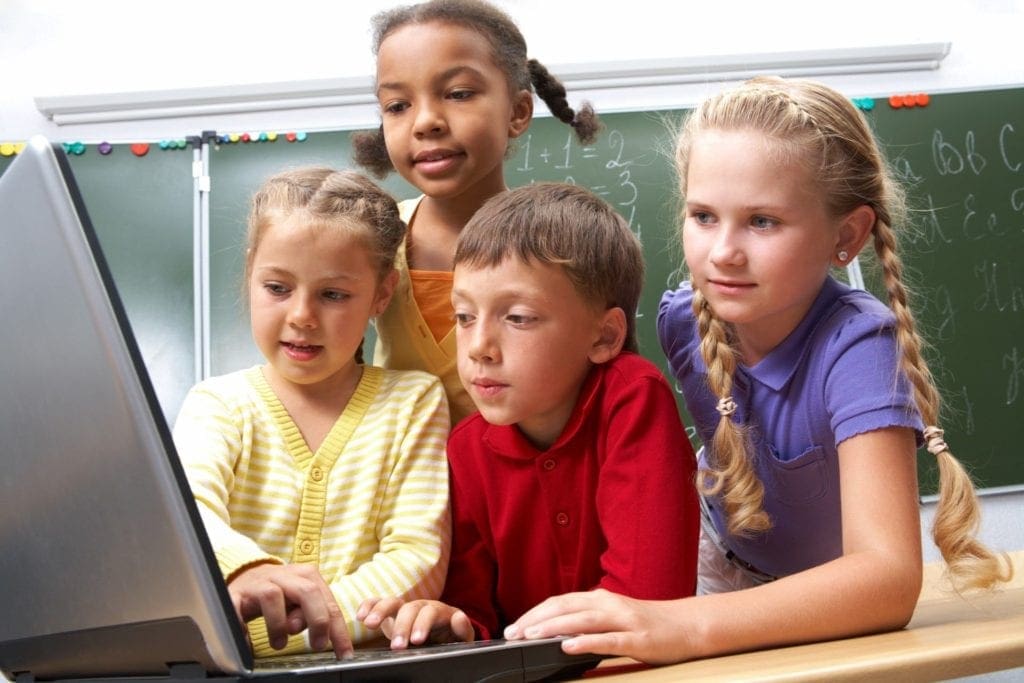 A group of kids in a classroom working together on a single laptop